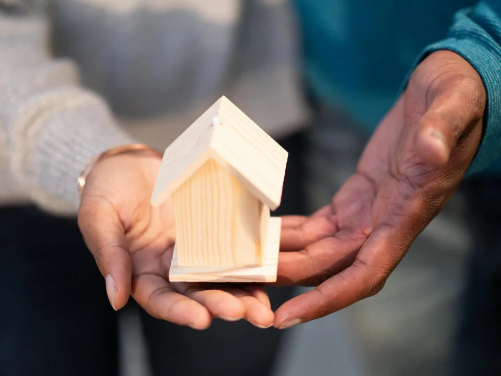 Hands holding a small wooden house model, symbolizing new home ownership and real estate transactions.